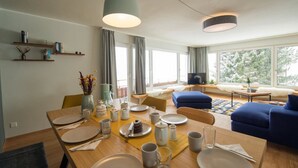Een moderne woonkamer met een eethoek, grote ramen en een televisie.