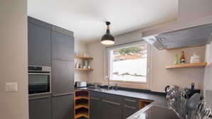 Een moderne keuken met grijze kastjes, een ingebouwde oven, een raam met uitzicht en een aanrecht met keukengerei.