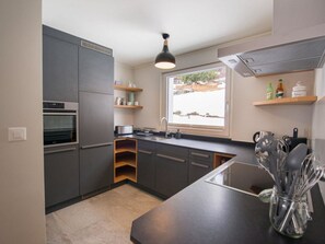 A modern kitchen with grey cabinets, a built-in oven, a window with a view, and a countertop with utensils. - Haus Mattern - Schafrügg Appartement/Fewo, Dusche und Bad, WC, 6-Bettwohnung by Interhome (Arosa)