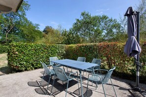 An outdoor patio with a table and chairs, surrounded by greenery and a hedge. - Gite louplàa – Renovated Farmhouse in a Rural Setting (Oloron-Sainte-Marie)