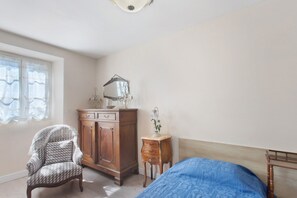 A bedroom with a bed, a wooden dresser, a chair, and a small table with a lamp.