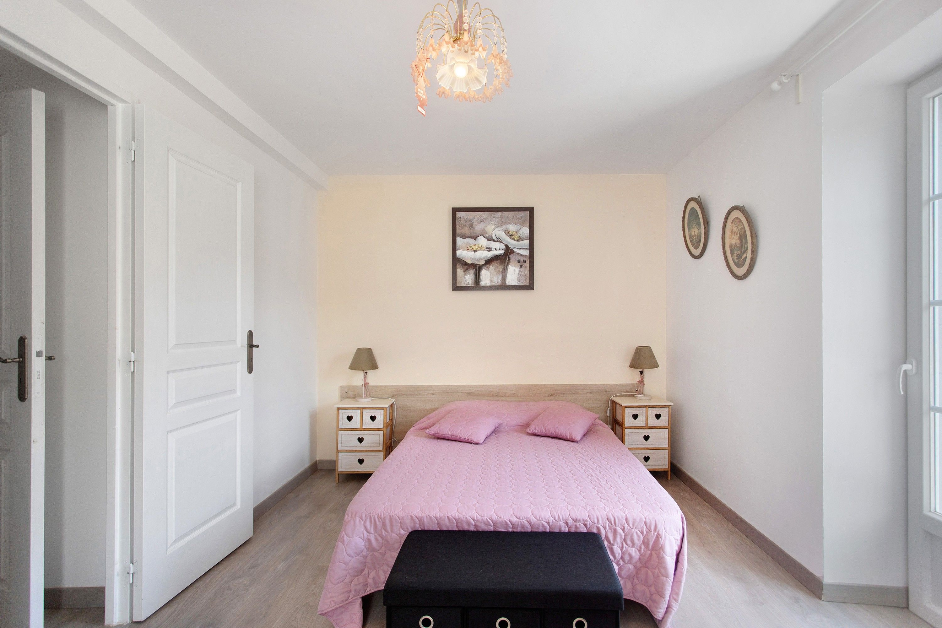 Une chambre à coucher comprenant un lit, des tables de chevet, un luminaire suspendu et des œuvres d’art murales.