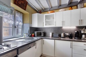 A modern kitchen with white cabinets, a stainless steel sink, a microwave, a kettle, and a coffee maker.