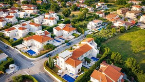 Vista aérea de un barrio residencial con casas modernas, una piscina y una calle.