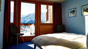 Ein Hotelzimmer mit Bett, zwei Stühlen, einem großen Fenster mit Bergblick und einer Tür.
