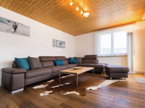 Ein modernes Wohnzimmer mit einem braunen Leder-Modulsofa, einem Holztisch und einem Kuhfellteppich.
