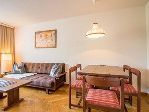 A cozy living area with a sofa, a dining table with chairs, a hanging light fixture, and a painting on the wall. - Rothornblick 46 by Arosa Holiday Appartement/Fewo,   Rothornblick 46 by Interhome (Arosa)