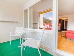 Ein Zimmer mit Esstisch und Stühlen, ein Fenster mit Bergblick und ein rotes Sofa im angrenzenden Raum.