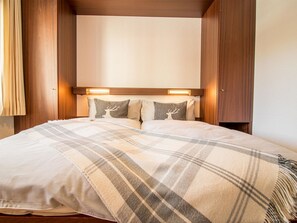 Ein Bett mit einer Karo-Decke, zwei Kissen mit Hirschmotiven und einem Kopfteil mit integrierter Beleuchtung.