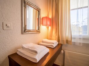 Ein Hotelbadezimmer mit einem Holzkosmetikschrank, einem Spiegel, einer Steckdose und einem Fenster mit Vorhängen.