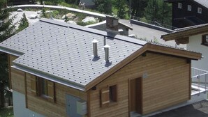 Eine Holzhütte mit geneigtem Dach, ein kleiner Anbau und ein gepflasterter Zugangsweg.
