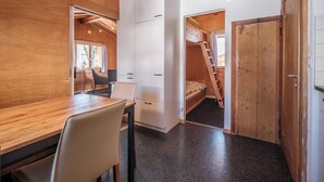 Ein kleines Zimmer mit Holztisch, Stühlen, einem Bett und einem Kleiderschrank.