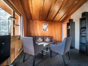 A cozy room with a wooden ceiling, a sofa with cushions, two armchairs, a small table, and a bookshelf. - Chalet Höckli 1 Appartement/Fewo,  , 6-Bettwohnung 6-Bettwohnung by Interhome (Arosa)