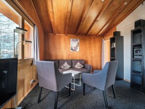 A cozy room with a wooden ceiling, a sofa, two chairs, a small table, and a bookshelf. - Chalet Höckli 1 Appartement/Fewo,  , 6-Bettwohnung 6-Bettwohnung by Interhome (Arosa)