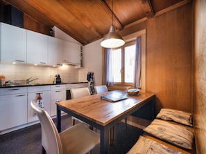 A compact kitchen with white cabinets, a wooden dining table, and a hanging pendant light. - Chalet Höckli 1 Appartement/Fewo,  , 6-Bettwohnung 6-Bettwohnung by Interhome (Arosa)