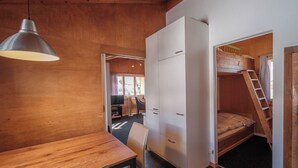 Ein kleines Zimmer mit einem Holztisch, einem einzelnen Stuhl, einem Kleiderschrank und einem Etagenbett mit einer Stehle.