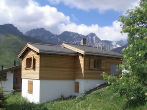 Un chalet en bois, doté d’un toit à pente, qui se dresse sur un fond de montagnes.