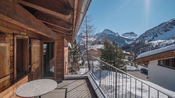 Ein Holzbalkon mit Tisch und Stühlen mit Blick auf eine verschneite Berglandschaft.