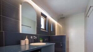 Une salle de bain moderne avec un meuble-lavabo bleu foncé, un lavabo blanc, un miroir, une petite plante en pot et un espace douche.