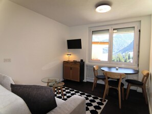 A compact living space with a sofa, a small round table, a cabinet, and a window with a mountain view. - Jäggi 35 by Arosa Holiday Appartement/Fewo, Bad, WC, 1 Schlafraum by Interhome (Arosa)