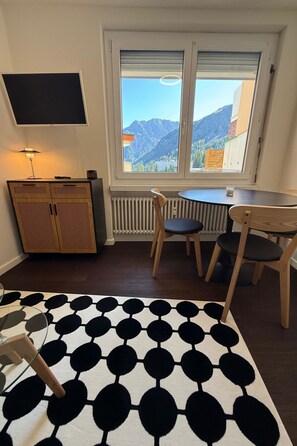 A room with a bed, a table, chairs, a TV, and a window with a mountain view. - Jäggi 35 by Arosa Holiday Appartement/Fewo, Bad, WC, 1 Schlafraum by Interhome (Arosa)