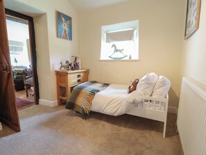Un dormitorio con cama, tocador, ventana con vistas y puerta que da a otra habitación.