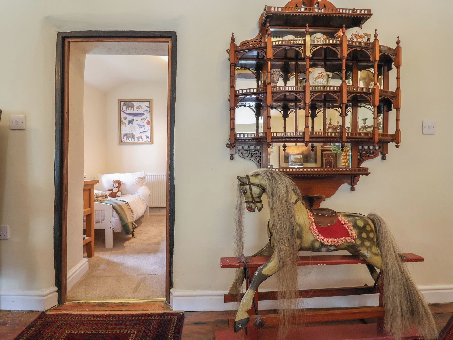 Quarto com um cavalinho de baloiço de madeira, um espelho e uma porta para outro espaço.