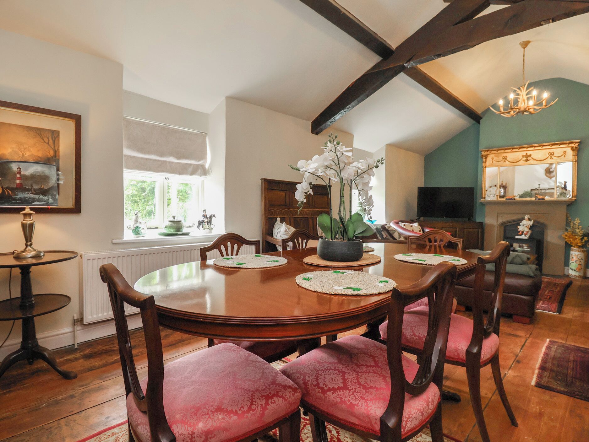 A dining area with a wooden table, red upholstered chairs, a potted orchid, and a chandelier.