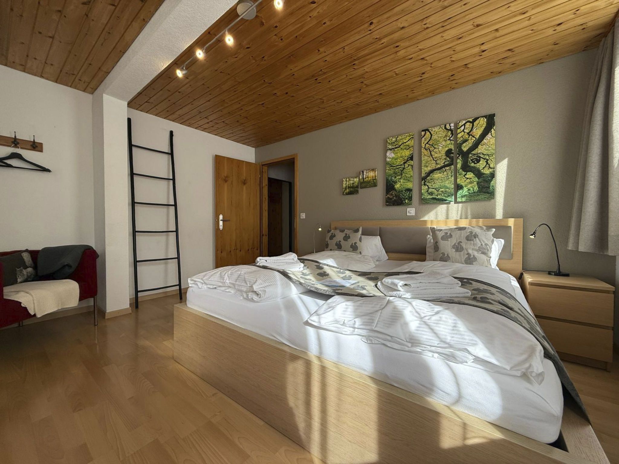 Une chambre à coucher avec un grand lit, un plafond en bois, une armoire, une table de chevet et un mur orné de trois tableaux.