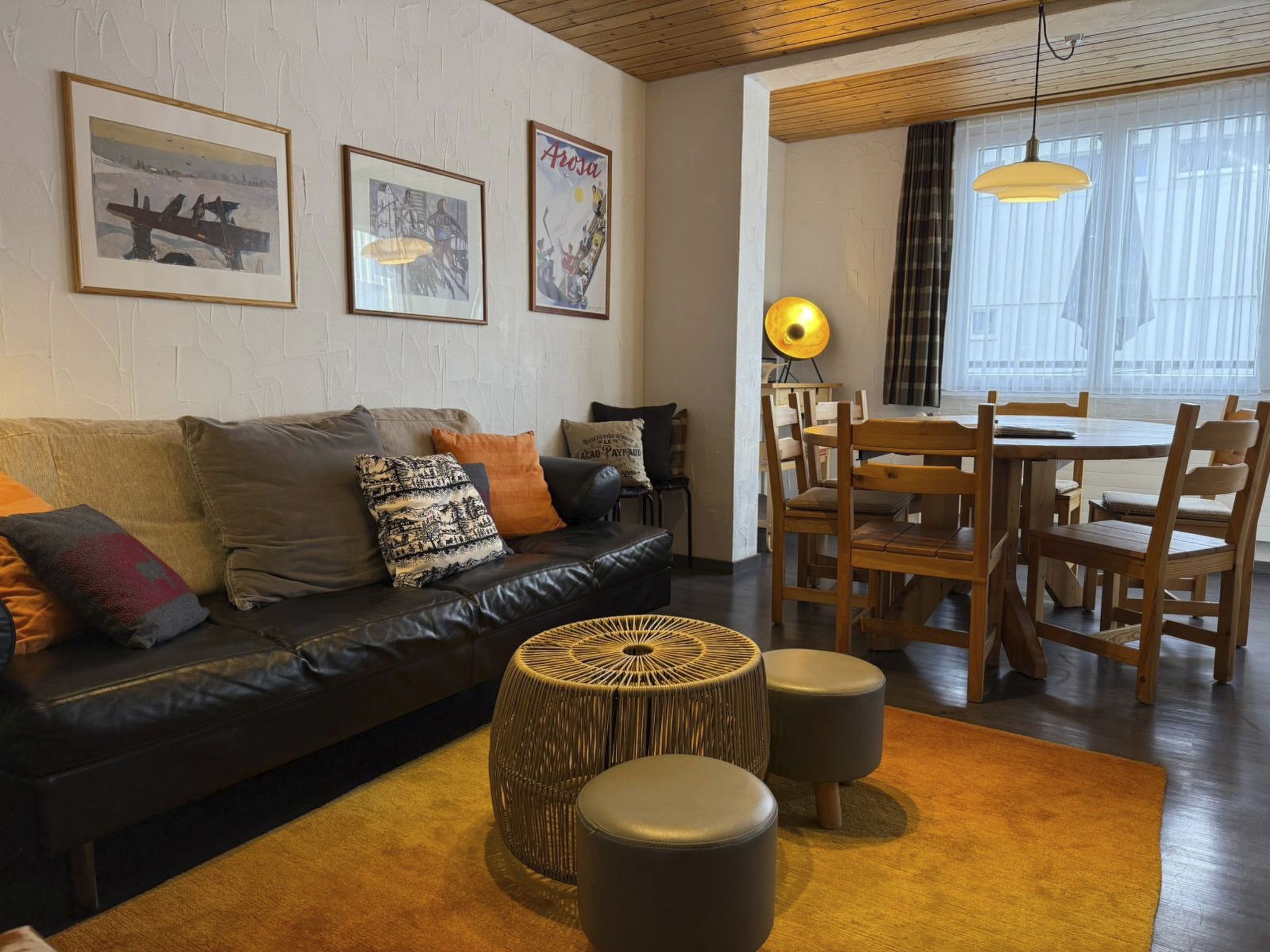 A furnished living room with a sofa, ottomans, a dining table with chairs, and wall art.