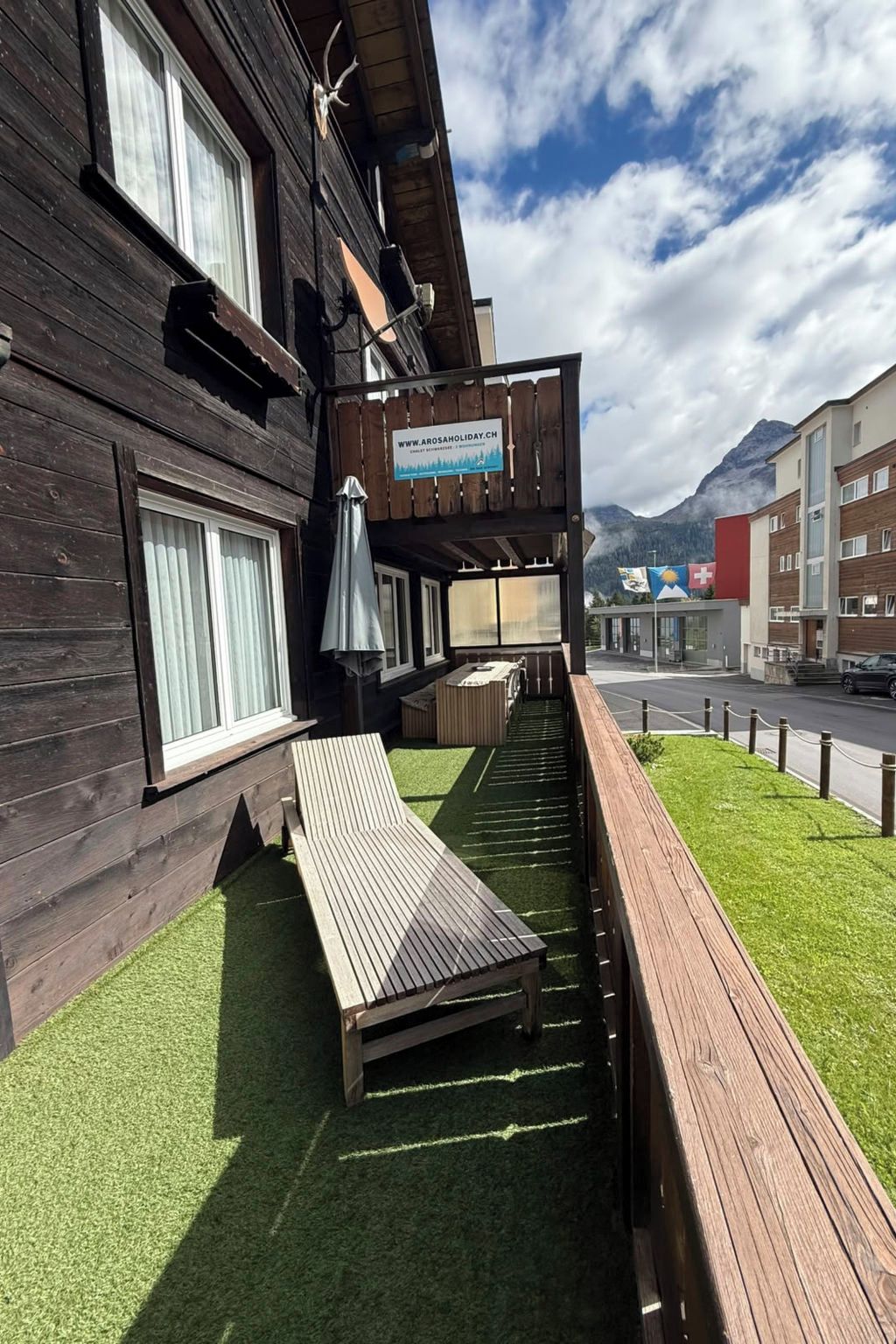 Ein Holzhaus mit Balkon, einem Schild mit einer Website-Adresse und einem Berg im Hintergrund.