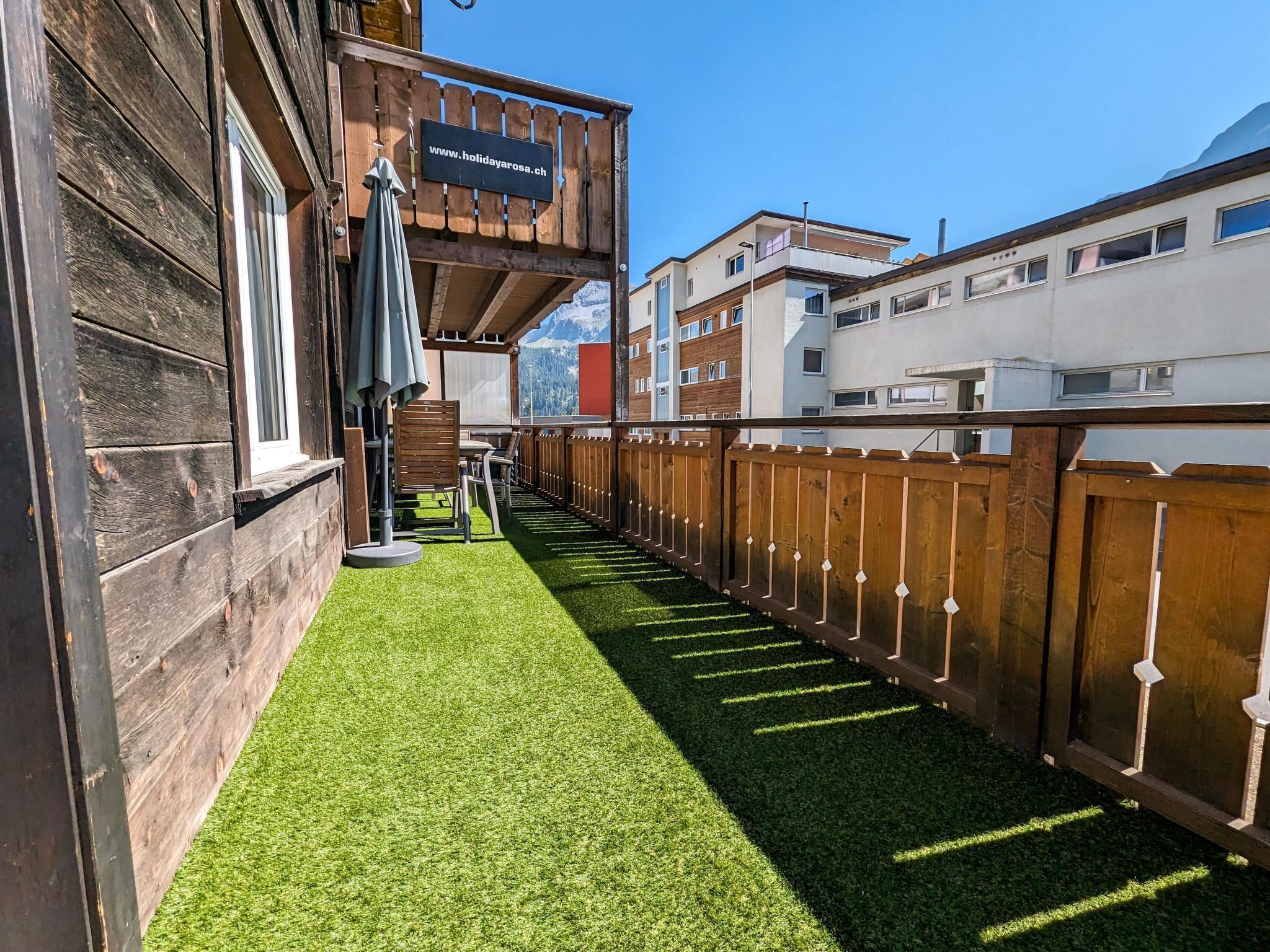 A wooden deck with artificial grass, a wooden fence, and a sign with a website address.