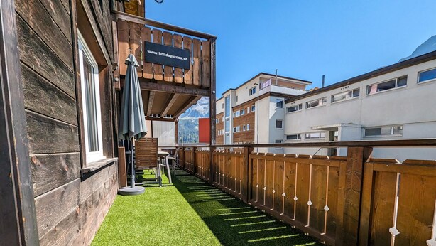 Une terrasse en bois recouverte de gazon synthétique, une clôture en bois et un panneau indiquant l’adresse d’un site web.