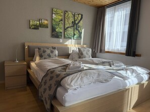 A neatly made bed with pillows and a blanket, a bedside table with a lamp, and a window with curtains. - Schwarzsee 1 by Arosa Holiday Appartement/Fewo,   Schwarzsee 1 by Interhome (Arosa)