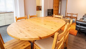 Un coin repas avec une grande table en bois entourée de chaises, un téléviseur et un canapé, dans une pièce dont le plafond et les murs sont en bois et peints en blanc.