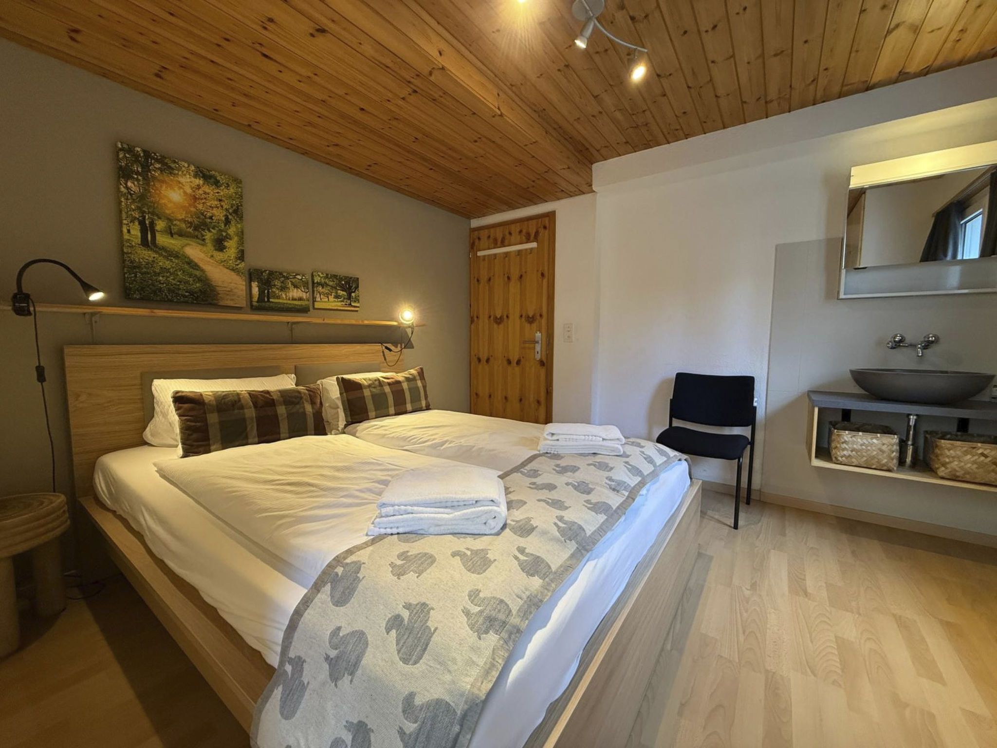 Ein Schlafzimmer mit Holzboden, einem Bett mit weißer Bettwäsche, einem Sessel, einem Nachttisch und einem wandmontierten Spiegel.