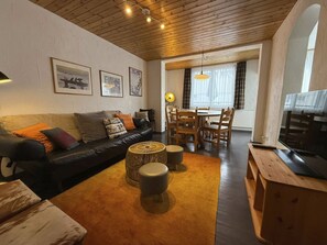 A living room with a sofa, ottomans, a coffee table, and a dining area with a table and chairs. - Schwarzsee 1 by Arosa Holiday Appartement/Fewo,   Schwarzsee 1 by Interhome (Arosa)