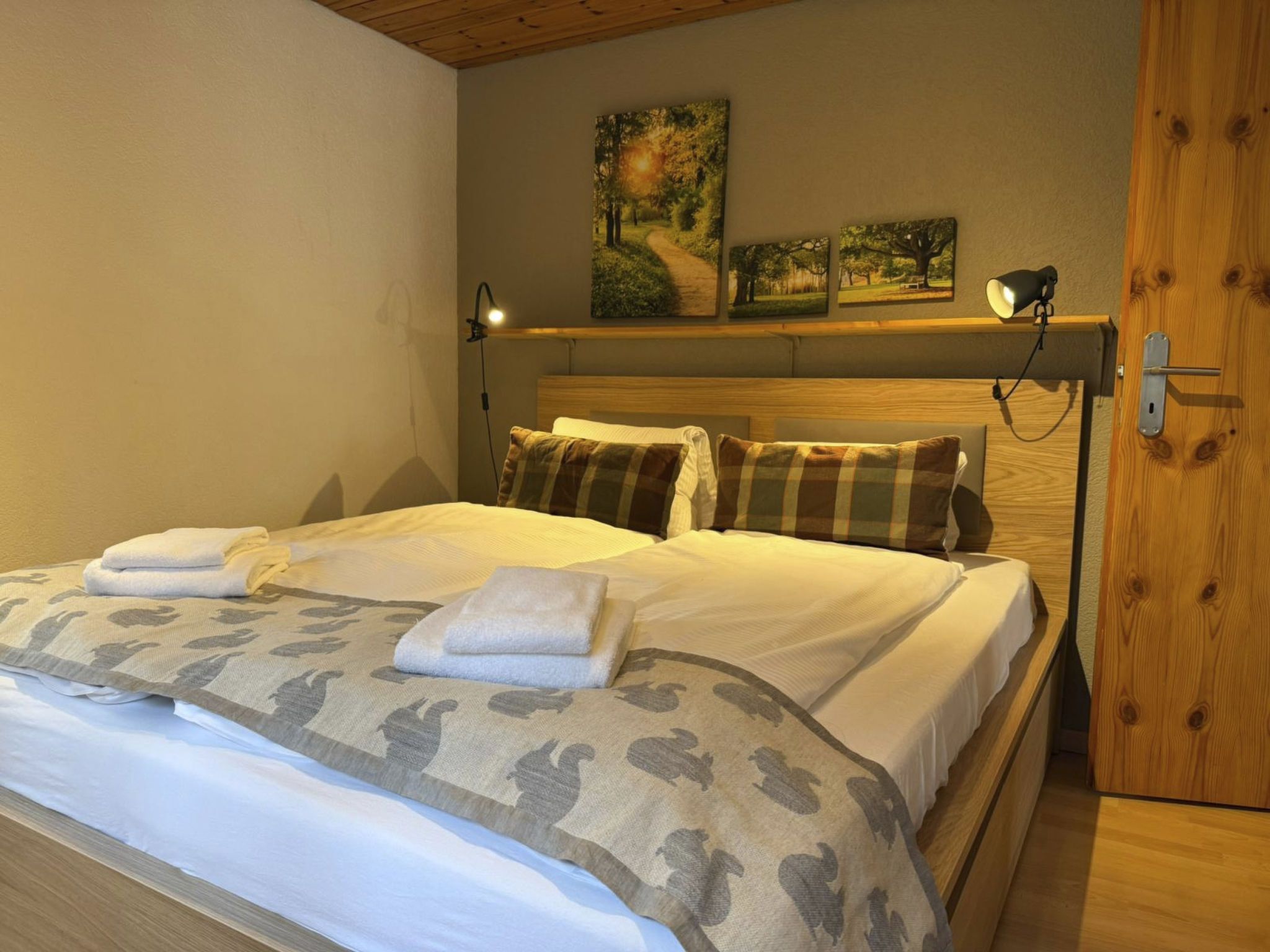 A neatly made bed with a patterned blanket and pillows, a bedside lamp, and a wooden headboard.