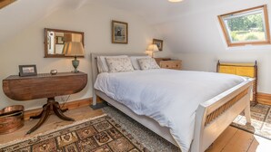 A bedroom with a bed, bedside tables, a mirror, a lamp, a picture frame, and a window. - Holiday Home With Sea Views In Llanfairfechan | Uwch-Y-Mor (Llanfairfechan)