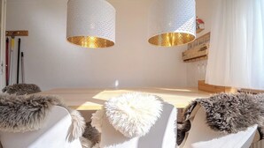 Ein Essbereich mit einem Holztisch, weißen Stühlen mit Felldecken und zwei Pendelleuchten mit strukturierter weißer Außenseite und goldenem Innenraum.