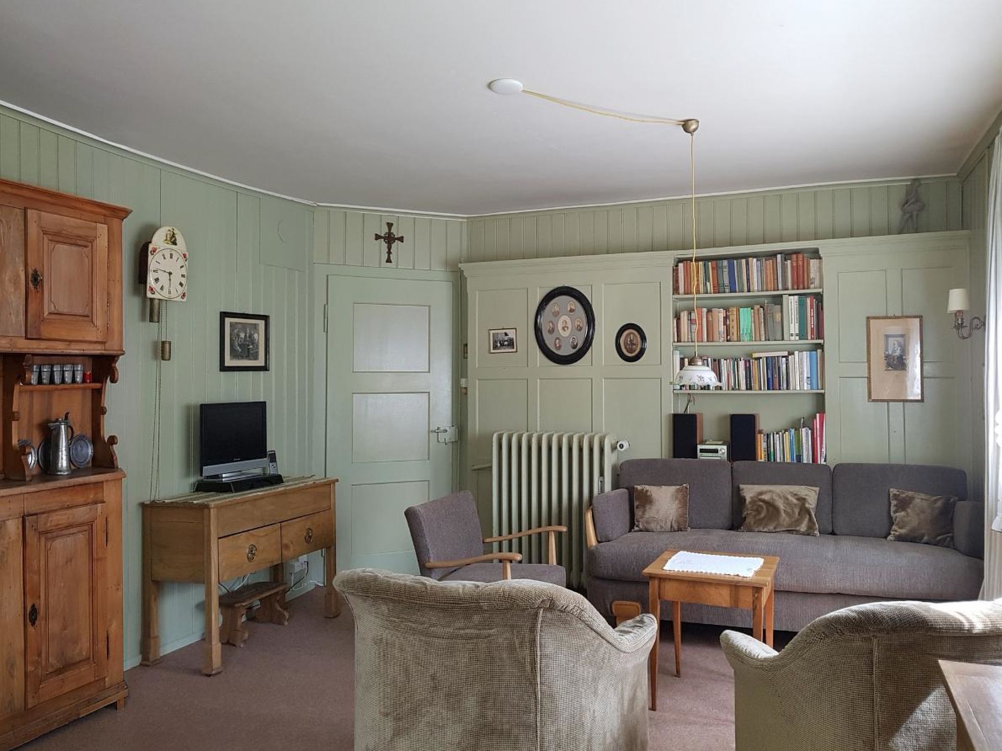 A living room with a sofa, armchairs, a wooden cabinet, a television, and a bookshelf.