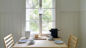 Ein Esstisch mit Stühlen, einer Karaffe, einem Brötchen, einer Kaffeemaschine und Tellern mit Tassen.