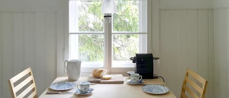 A dining table with chairs, a pitcher, a bread roll, a coffee maker, and plates with cups.