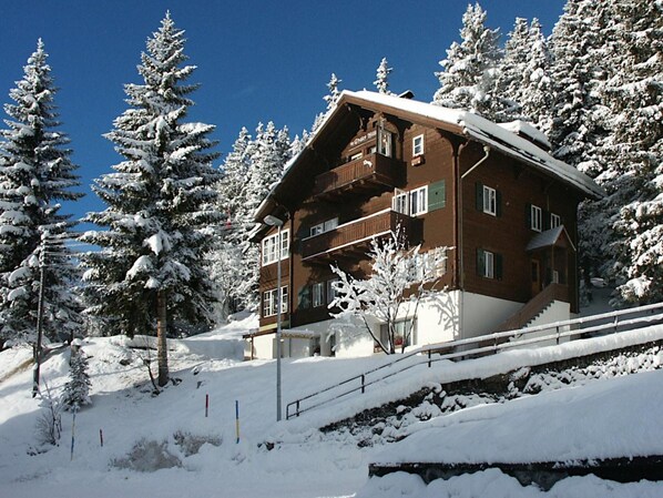 Un chalet en bois doté d’un balcon, entouré d’arbres couverts de neige.