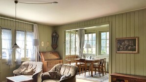 Ein Zimmer mit einem Esstisch, zwei Sesseln, einem Sofa, einer Holzkommode und einem Bild an der Wand.
