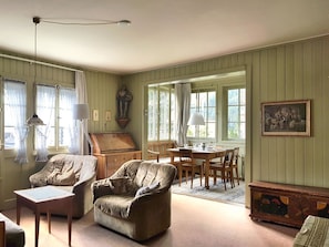 Ein Zimmer mit einem Esstisch, zwei Sesseln, einem Sofa, einer Holzkommode und einem Bild an der Wand.