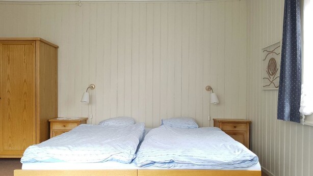 Ein Doppelbett mit Holzrahmen, zwei Nachttische, ein Kleiderschrank und eine Wandlampe.