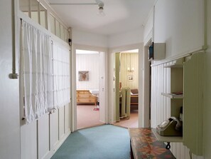 Ein schmaler Flur mit einem Bett im Hintergrund, einem Heizkörper und einem Regal mit Gegenständen auf der rechten Seite.