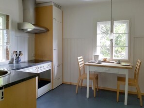 A kitchen with a stove, oven, and cabinets, a dining table with chairs, and a window with a view of trees. - Chalet Willi-2.OG Appartement/Fewo, Dusche und Bad, WC, 6-Bettwohnung by Interhome (Arosa)
