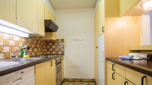 Eine schmale Küche mit Holzschränken, einer gefliesten Spritzschutzwand, einem Geschirrspüler und einer Arbeitsplatte mit Spüle.